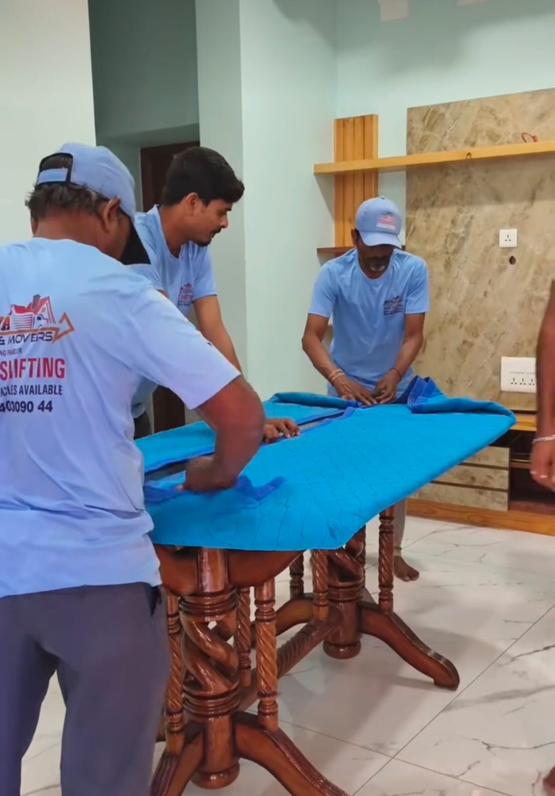 Uniformed Aadhya crew wrapping a dining table in padded quilted covers